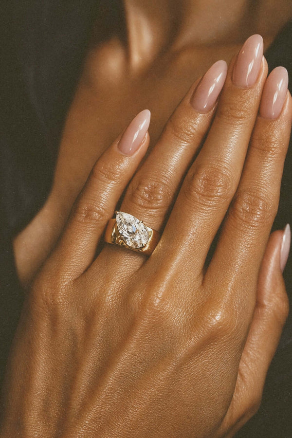 A Wonderful Thing Tilted Pear Cigar Band Ring worn on a hand with elegant nails, showcasing its cubic zirconia and gold finish.
