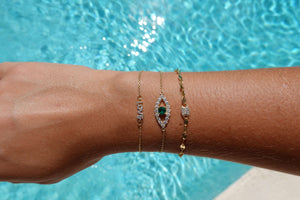 Divinely Protected Evil Eye Bracelet displayed on a wrist near a pool, showcasing its elegant design and green pendant.
