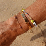 Be A Lover Pink Heart Bracelet shown with other bangles on a wrist against a sandy background.