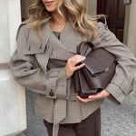 Woman wearing a stylish checkered jacket and holding a brown handbag.
