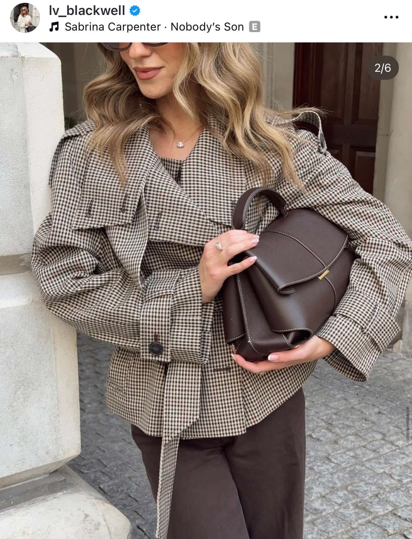Woman wearing a stylish checkered jacket and holding a brown handbag.