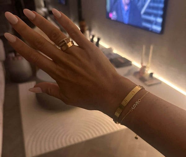 For The Lovers Gold L-O-V-E Bracelet showcased elegantly on a hand with stylish rings.