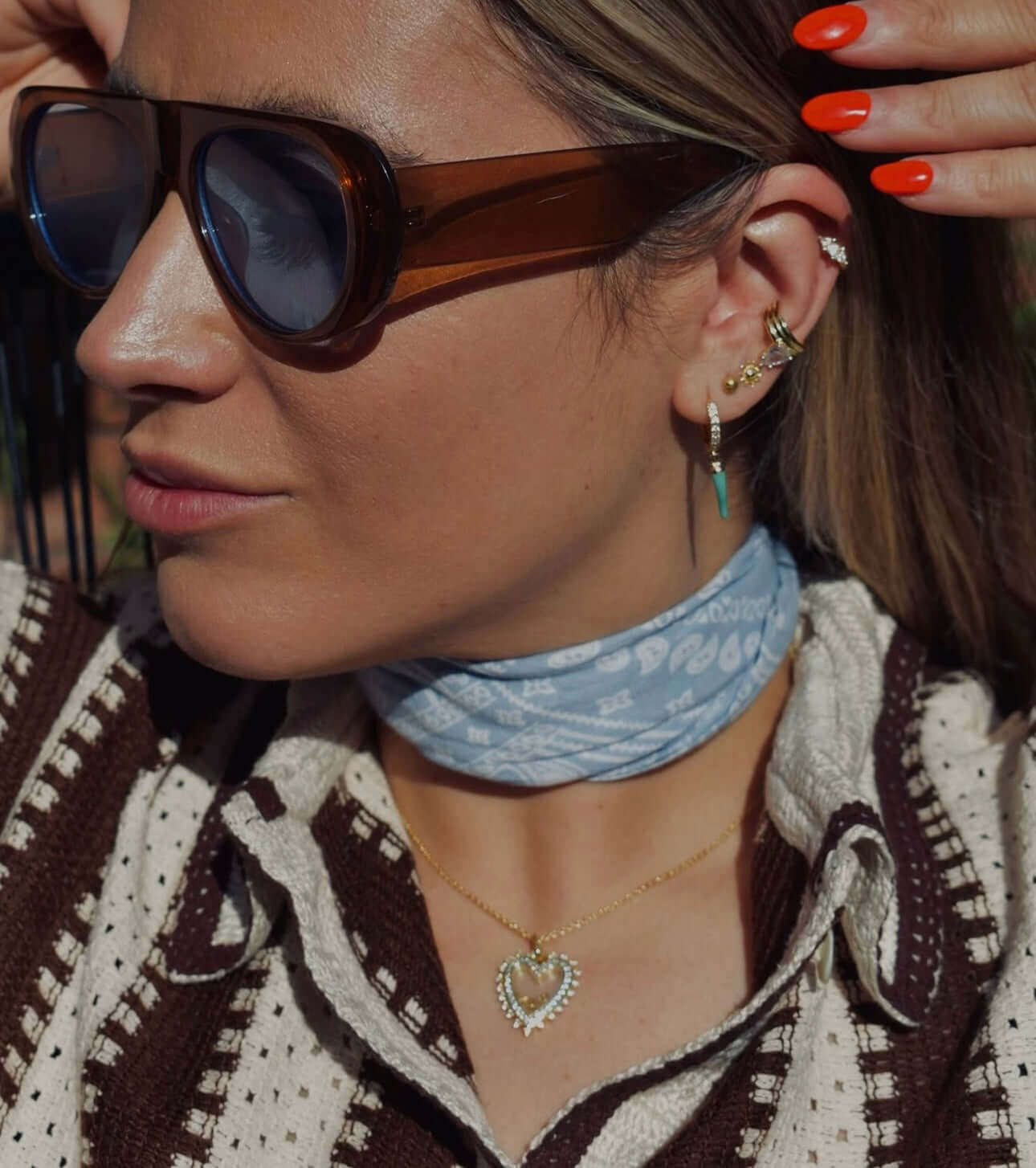 Woman wearing sunglasses and a light blue scarf showcasing the Eyes On Me Gold Ear Cuff With Pear Stone.