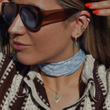 Woman wearing sunglasses and a light blue scarf showcasing the Eyes On Me Gold Ear Cuff With Pear Stone.