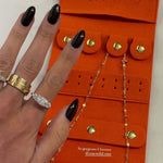 Yes You Can Gold Necklace displayed in an orange jewelry organizer with stylish rings and a hand with black nail polish.