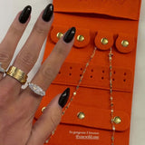 Yes You Can Gold Necklace displayed in an orange jewelry organizer with stylish rings and a hand with black nail polish.