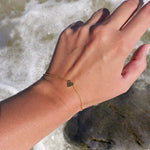 She's So Lucky Black Heart Bracelet worn on a hand by the ocean, showcasing the black CZ heart pendant and adjustable chain.