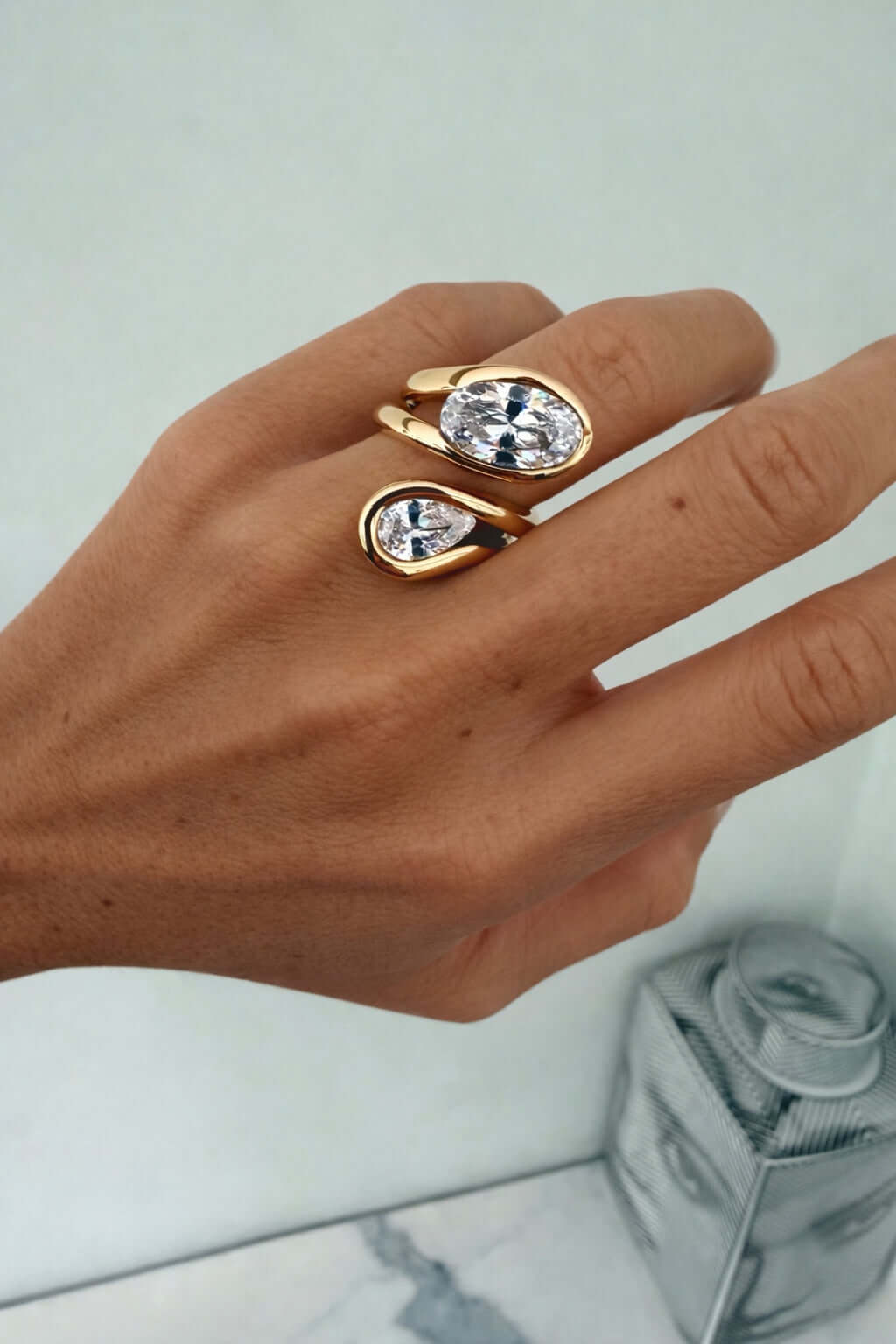 Close-up of a hand wearing the Can’t Compare Ring featuring two light-catching stones in a sculptural design.